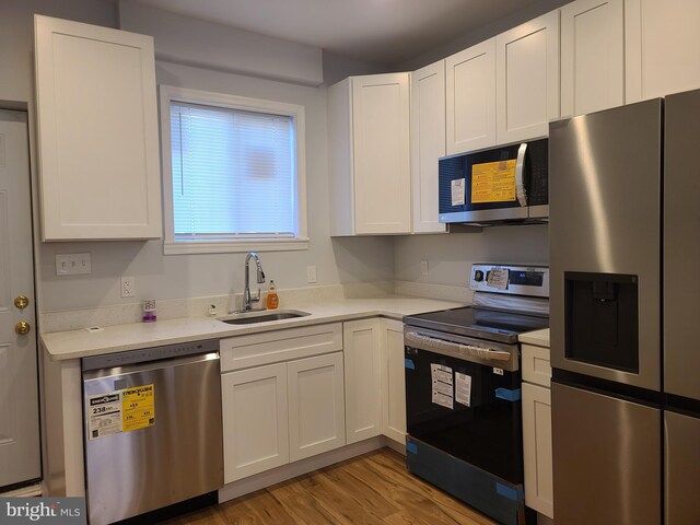 kitchen featuring a sink, light wood-style floors, white cabinets, light countertops, and appliances with stainless steel finishes