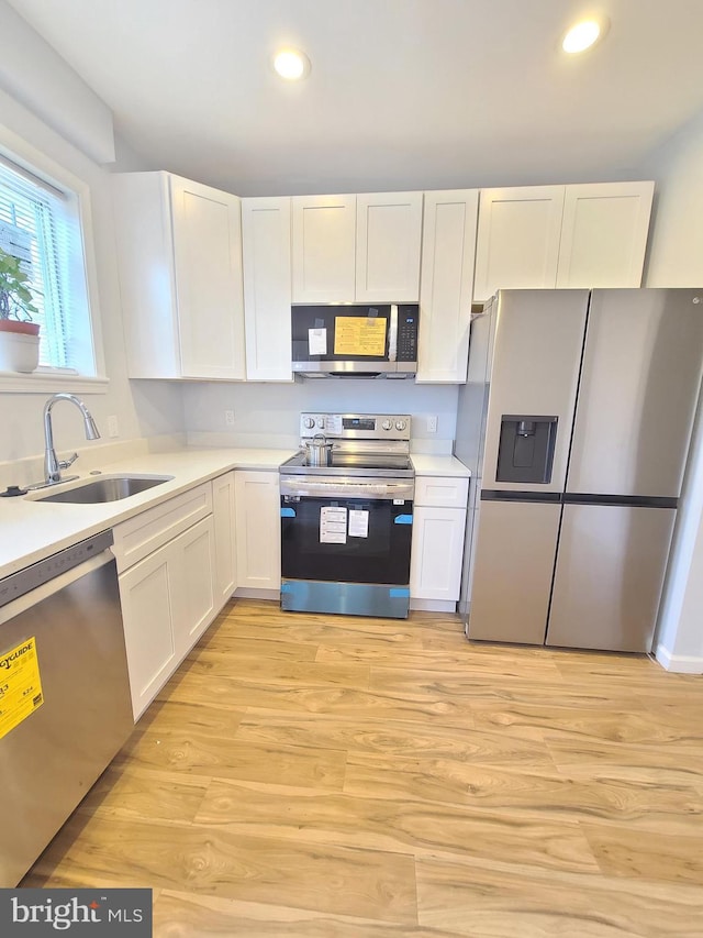 kitchen with white cabinets, light wood-style flooring, stainless steel appliances, light countertops, and a sink