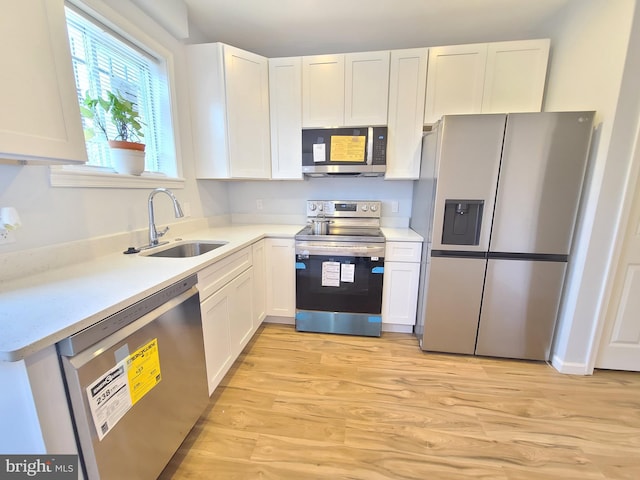 kitchen with stainless steel appliances, white cabinets, a sink, and light wood finished floors