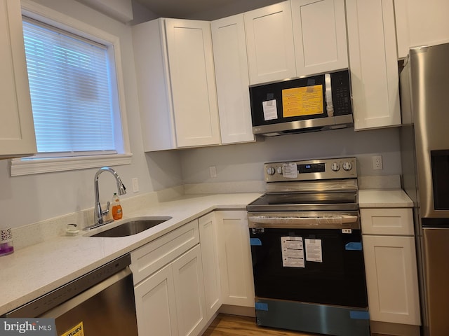 kitchen with light countertops, appliances with stainless steel finishes, a sink, and white cabinets