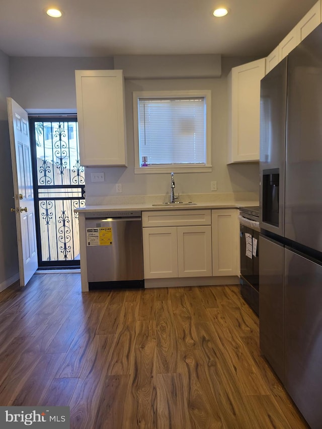 kitchen with dark wood-style floors, stainless steel appliances, light countertops, white cabinetry, and a sink