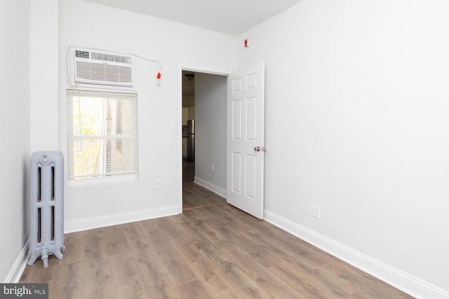 unfurnished room featuring an AC wall unit, light hardwood / wood-style flooring, and radiator heating unit