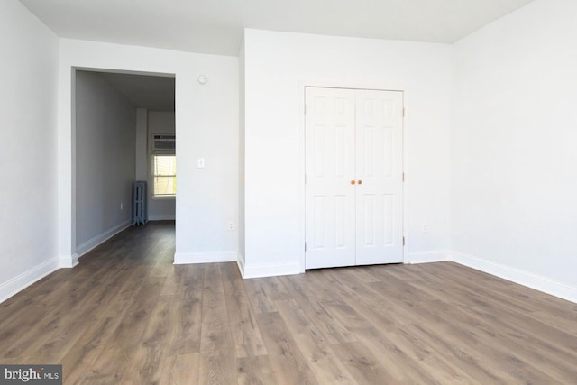 unfurnished bedroom featuring a closet, radiator heating unit, and dark hardwood / wood-style flooring