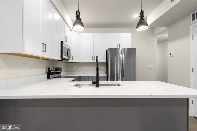 kitchen with light stone countertops, appliances with stainless steel finishes, pendant lighting, and white cabinets