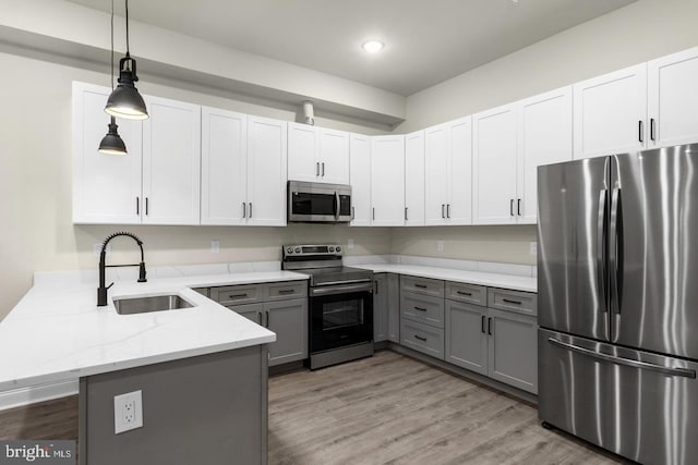 kitchen with appliances with stainless steel finishes, kitchen peninsula, white cabinets, and decorative light fixtures