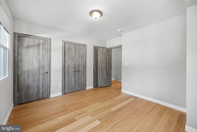 unfurnished bedroom with light hardwood / wood-style flooring and multiple closets