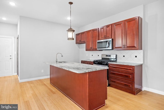 kitchen with appliances with stainless steel finishes, light stone counters, hanging light fixtures, and light hardwood / wood-style floors