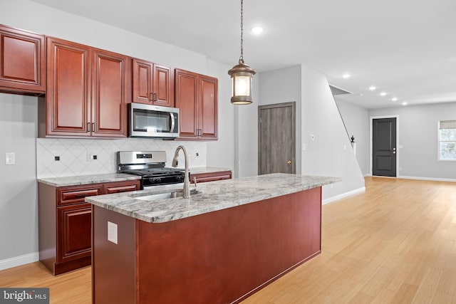 kitchen with light hardwood / wood-style floors, appliances with stainless steel finishes, pendant lighting, and light stone counters