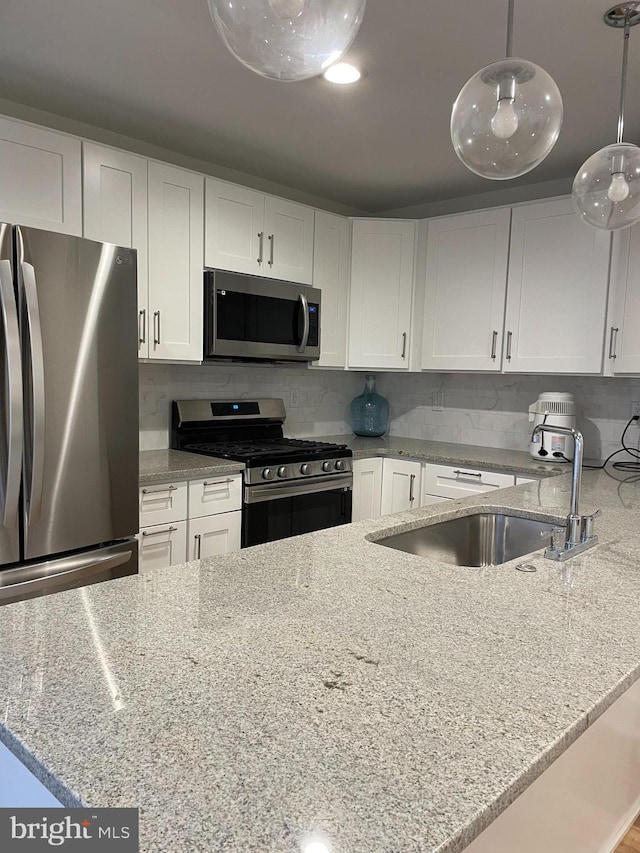 kitchen with appliances with stainless steel finishes, white cabinets, decorative light fixtures, and light stone counters