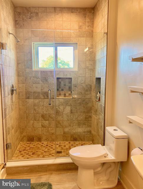 bathroom featuring toilet, an enclosed shower, and wood-type flooring