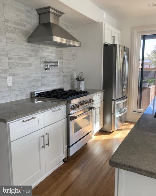 kitchen featuring white cabinets, tasteful backsplash, appliances with stainless steel finishes, dark wood-type flooring, and wall chimney exhaust hood