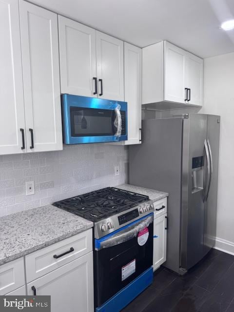 kitchen featuring dark wood-type flooring, tasteful backsplash, light stone counters, white cabinets, and appliances with stainless steel finishes