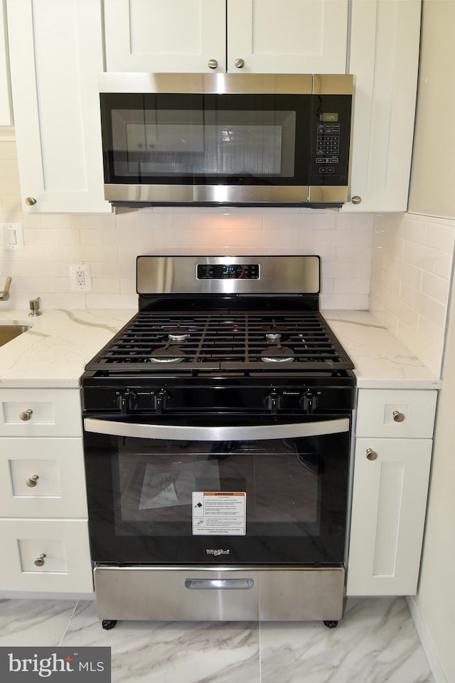 kitchen with light stone counters, stainless steel appliances, backsplash, and white cabinets