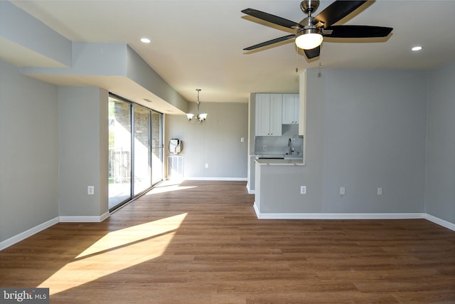 unfurnished living room featuring hardwood / wood-style flooring, sink, and ceiling fan with notable chandelier