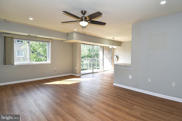 spare room with a healthy amount of sunlight, ceiling fan with notable chandelier, and hardwood / wood-style floors