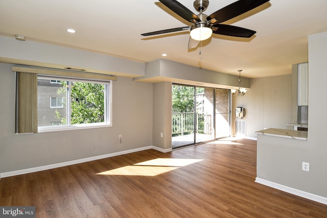 unfurnished living room featuring a healthy amount of sunlight, wood-type flooring, and ceiling fan with notable chandelier