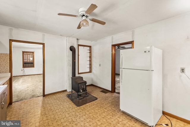 kitchen with a wood stove, white fridge, light colored carpet, and ceiling fan