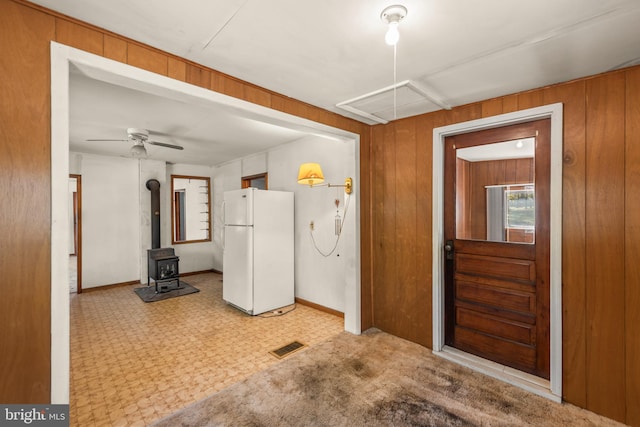 kitchen featuring a wood stove, ceiling fan, wooden walls, white fridge, and light colored carpet