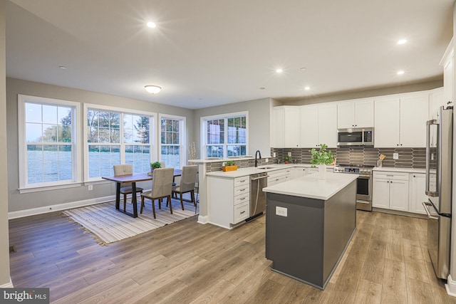 kitchen with a kitchen island, stainless steel appliances, backsplash, light wood-type flooring, and white cabinetry