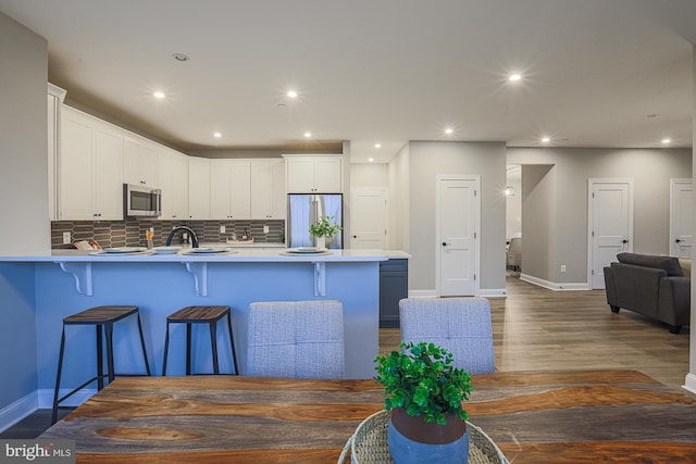 kitchen with kitchen peninsula, white cabinets, dark hardwood / wood-style flooring, a kitchen breakfast bar, and stainless steel appliances