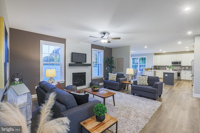 living room with a fireplace, light wood-type flooring, and ceiling fan