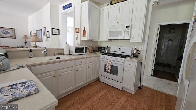 kitchen with white cabinetry, sink, hardwood / wood-style floors, and white appliances