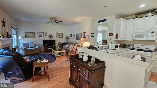 kitchen with white appliances, kitchen peninsula, white cabinetry, light hardwood / wood-style floors, and ceiling fan