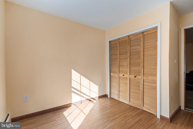 unfurnished bedroom with a closet, baseboard heating, and wood-type flooring