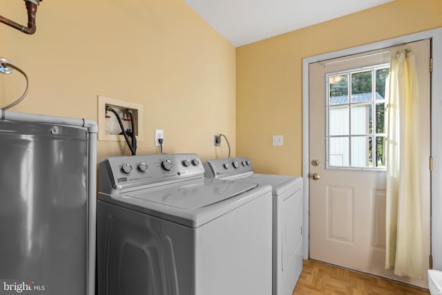 clothes washing area featuring water heater, washing machine and dryer, and light parquet flooring