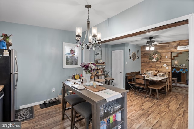 dining room featuring wood finished floors, ceiling fan with notable chandelier, and wooden walls