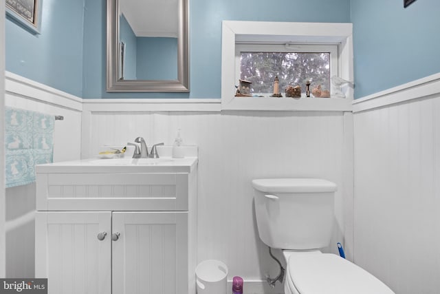 bathroom featuring toilet, vanity, wainscoting, and a decorative wall