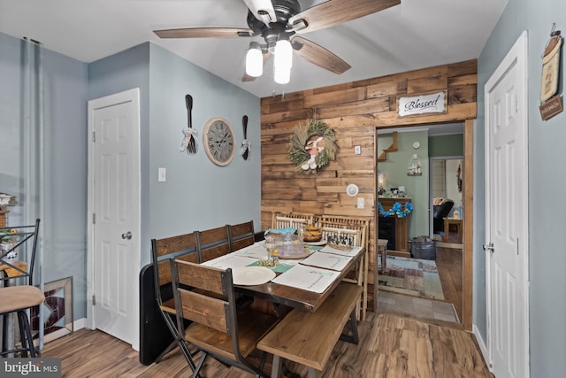dining area featuring wood walls, wood finished floors, a ceiling fan, and baseboards