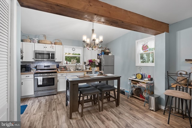 kitchen featuring beamed ceiling, an inviting chandelier, stainless steel appliances, and light wood-style floors