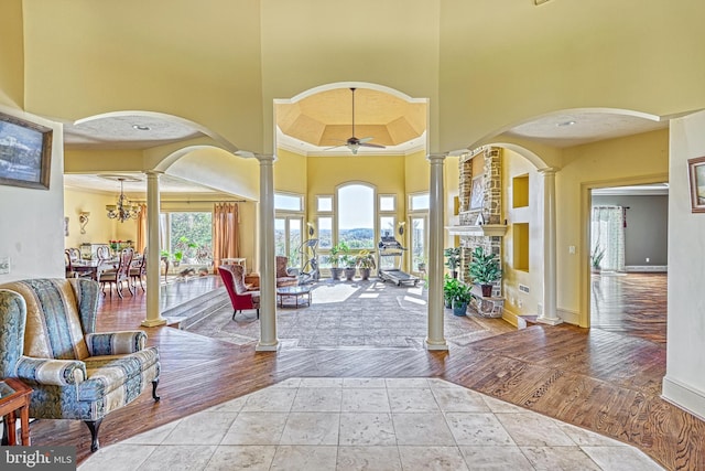 foyer entrance featuring decorative columns, ceiling fan, a towering ceiling, and light hardwood / wood-style flooring