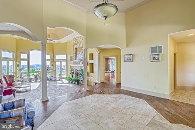 entryway with ornate columns, a stone fireplace, crown molding, light wood-type flooring, and a towering ceiling