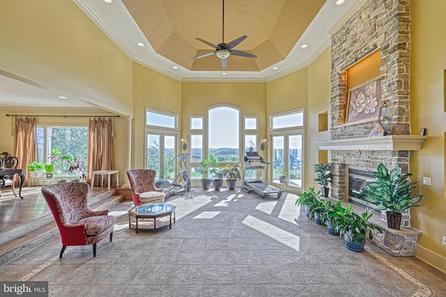 living room with a towering ceiling, ornamental molding, a fireplace, and ceiling fan