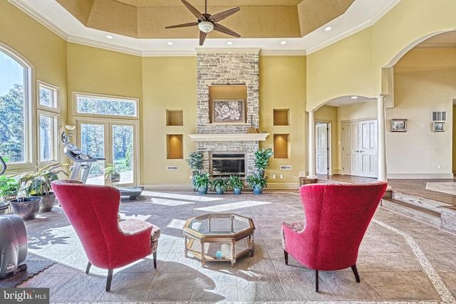 living room featuring a high ceiling, a fireplace, crown molding, and decorative columns