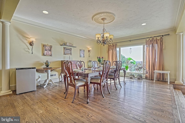 dining area with ornate columns, wood-type flooring, crown molding, a chandelier, and a textured ceiling