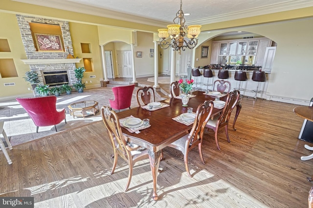 dining area featuring ornamental molding, hardwood / wood-style floors, a stone fireplace, and a chandelier