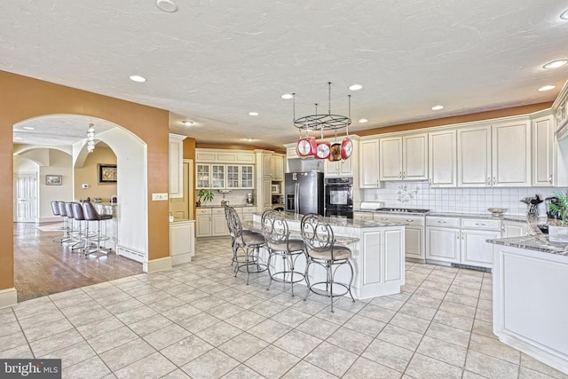 kitchen featuring light stone countertops, backsplash, a breakfast bar, a center island with sink, and stainless steel refrigerator with ice dispenser