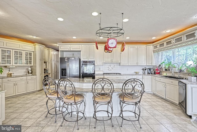 kitchen featuring light stone countertops, sink, light tile patterned flooring, black appliances, and a center island