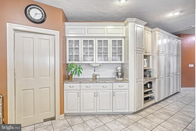 bar featuring decorative backsplash, white cabinetry, a textured ceiling, and light tile patterned floors