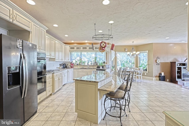 kitchen with cream cabinets, light stone counters, stainless steel appliances, decorative light fixtures, and a center island