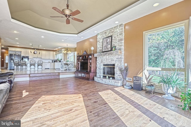 unfurnished living room featuring hardwood / wood-style floors, a fireplace, ceiling fan with notable chandelier, and a raised ceiling