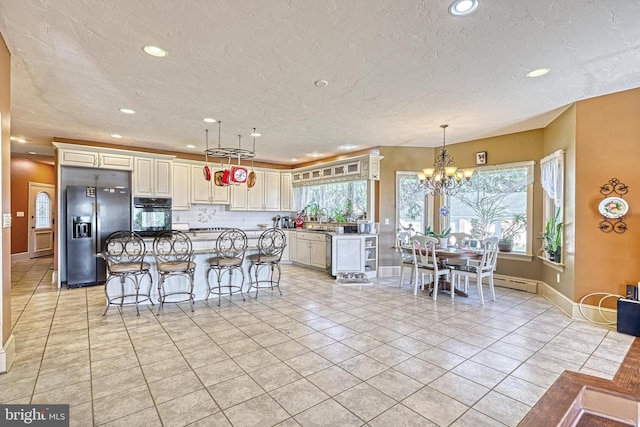 kitchen featuring black oven, light tile patterned floors, a kitchen island, and stainless steel fridge with ice dispenser