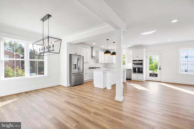 kitchen featuring wall chimney range hood, a healthy amount of sunlight, appliances with stainless steel finishes, and white cabinetry