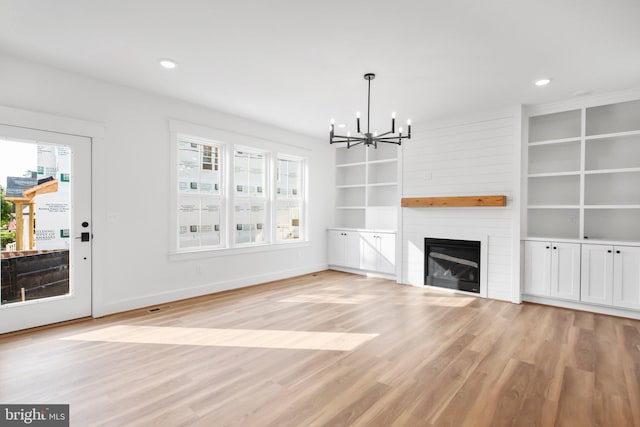 unfurnished living room with light hardwood / wood-style flooring, a notable chandelier, and a fireplace