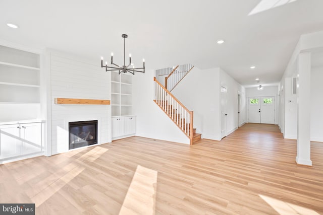 unfurnished living room featuring light hardwood / wood-style floors, a notable chandelier, a large fireplace, and built in shelves