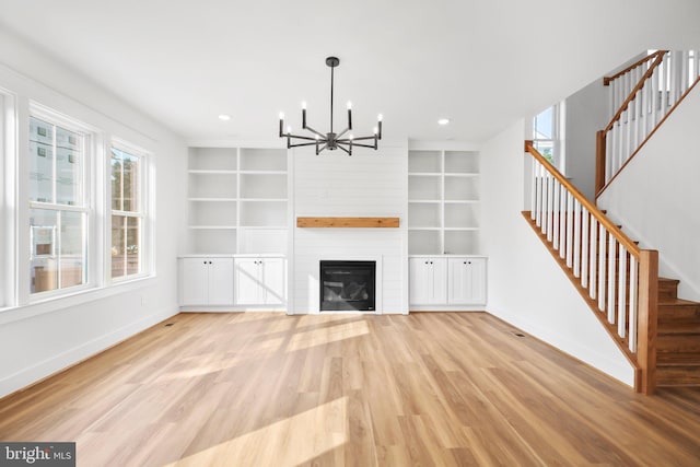 unfurnished living room featuring light hardwood / wood-style flooring, a chandelier, a large fireplace, and built in features