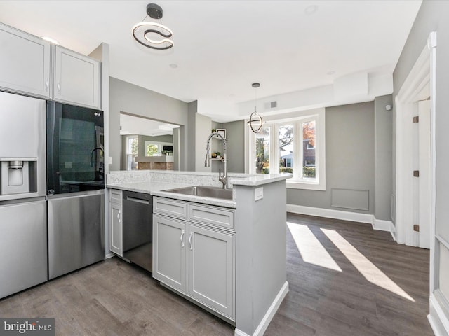 kitchen with dark hardwood / wood-style floors, kitchen peninsula, sink, appliances with stainless steel finishes, and light stone counters